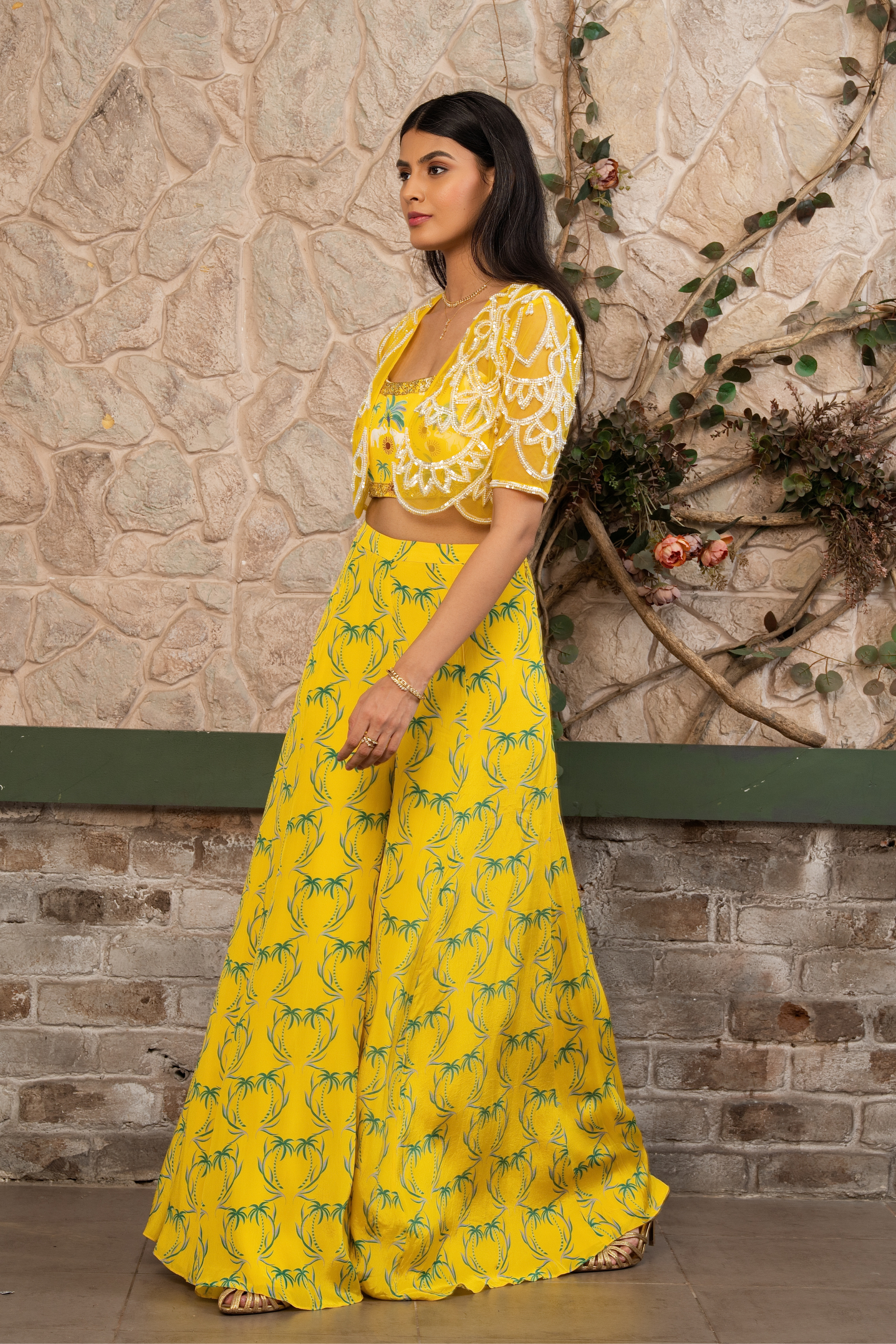 Woman wearing a yellow printed bustier with flowing sharara pants and a hand-embroidered cape in Senren's signature Nomad's Tale bohemian print.