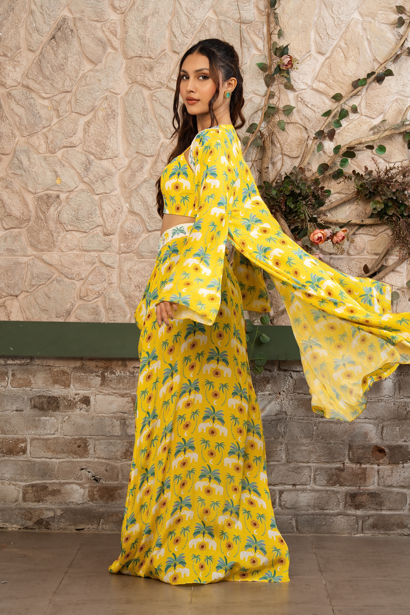 Woman wearing a yellow  printed draped skirt set with a bustier blouse and embroidered cape in Senren's signature  bohemian print against a textured wall.