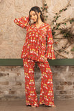 Woman wearing a red printed designer co-ord set with a pleated V-neck tunic and flared pants featuring tropical and elephant motifs by Senren.