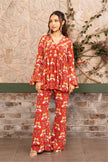 Woman wearing a red printed designer co-ord set with a pleated V-neck tunic and flared pants featuring tropical and elephant motifs by Senren.