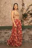 A woman wearing a sleeveless red corset blouse with a gold and white elephant print, standing against a rustic stone wall with climbing vines.