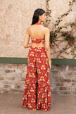 A woman stands with her back to the camera wearing a red halter neck printed co-ord set with wide-leg sharara pants in Senren's signature bohemian print.
