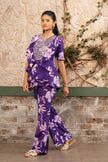 Woman wearing a purple floral printed embroidered ruffle peplum top with flared trousers in a luxury co-ord set by Senren.