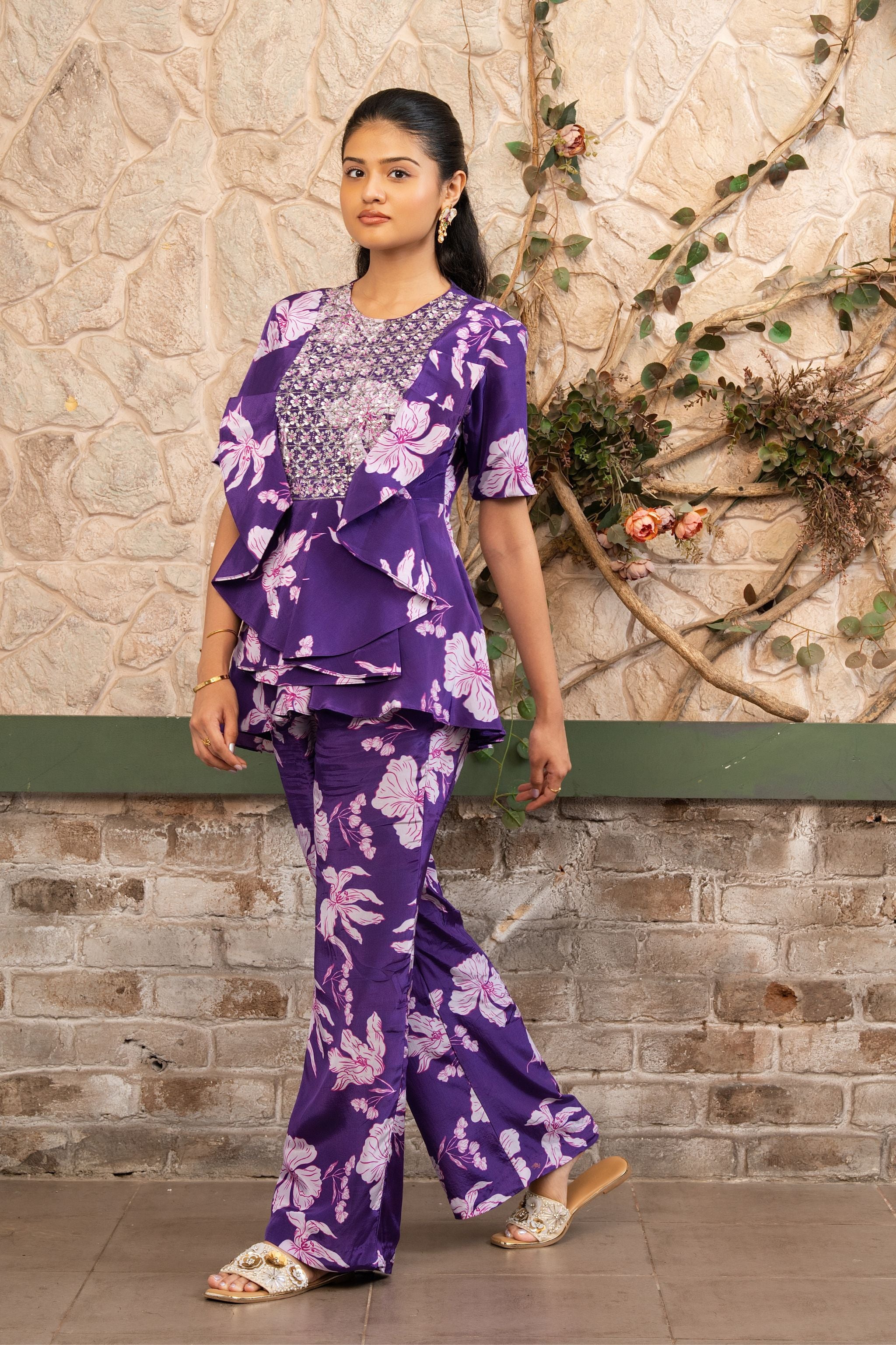 Woman wearing a purple floral printed embroidered ruffle peplum top with flared trousers in a luxury co-ord set by Senren.