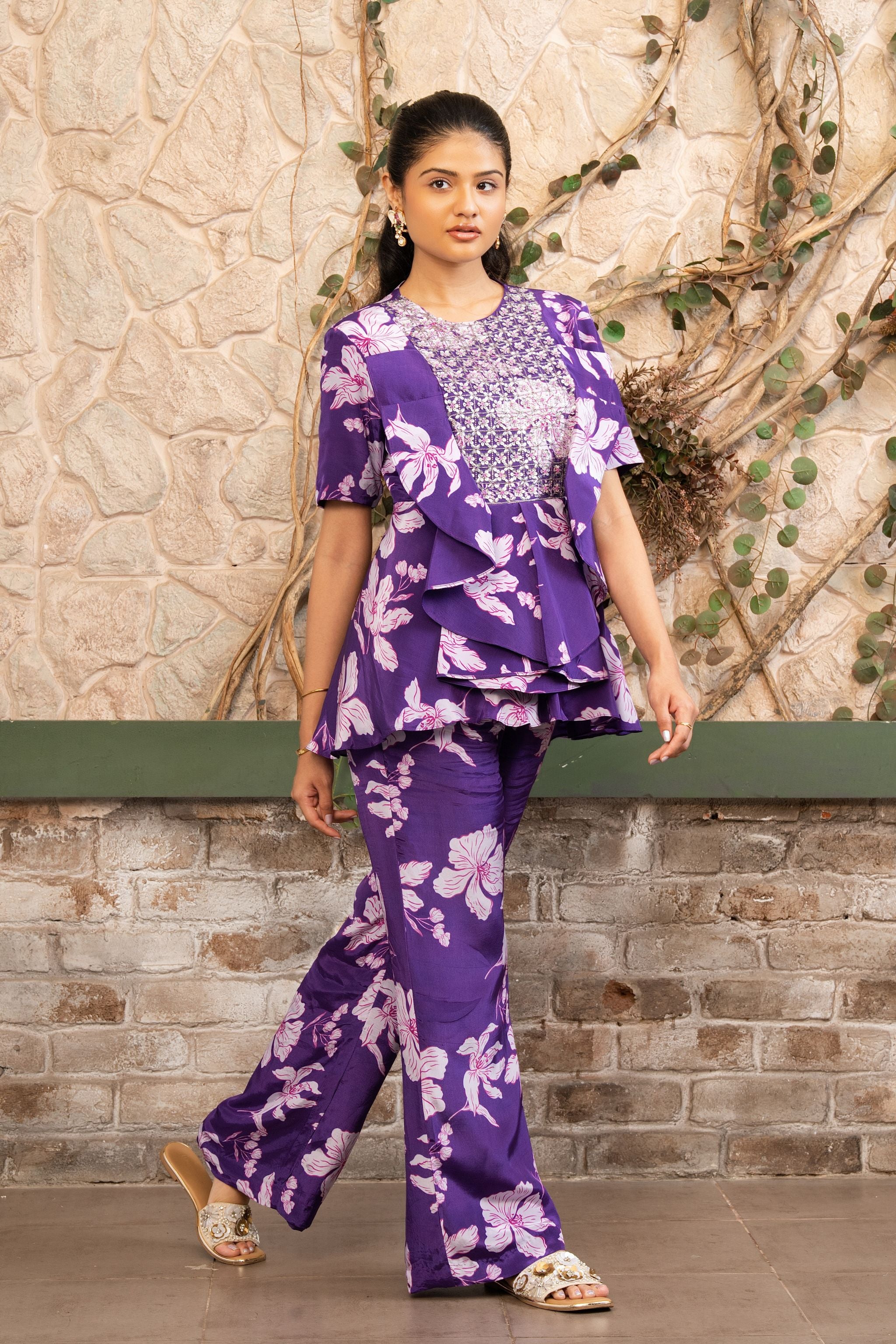 Woman wearing a purple floral printed embroidered ruffle peplum top with flared trousers in a luxury co-ord set by Senren.